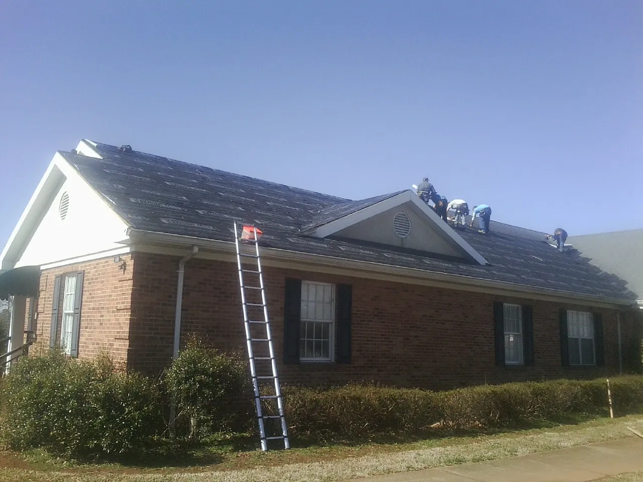 Crew tearing shingles off a brick ranch roof with a ladder set — Metal Roof Repair work by our crew in Gordonsville