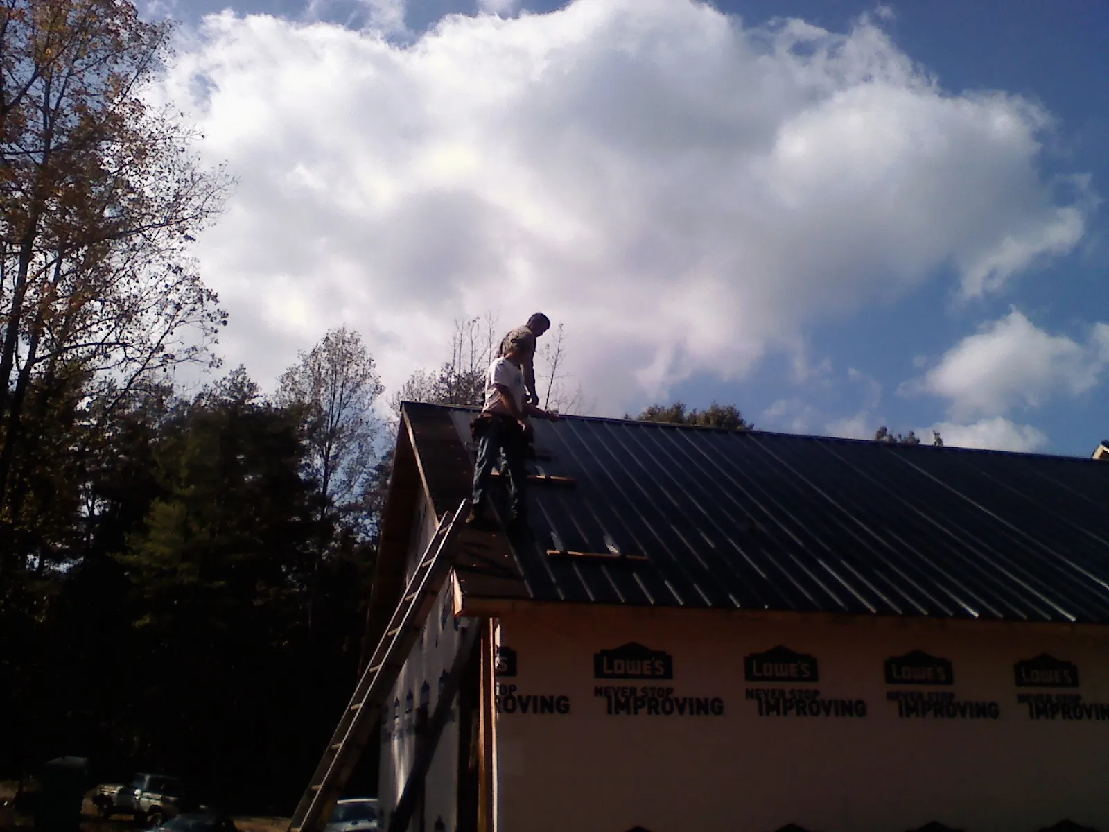 Roofer fastening dark metal panels high against a cloudy sky, from a Roof Inspection job in Gordonsville