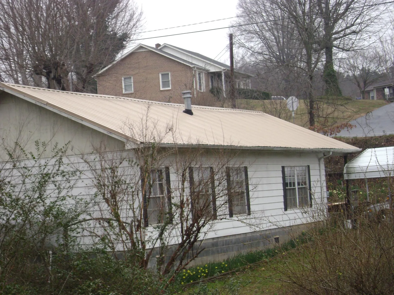 Tan metal roof on a white sided house set into a hillside — Commercial Roofing by Roofing Brothers in Gordonsville
